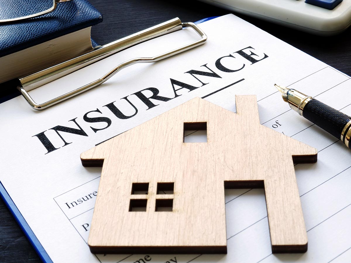 Home insurance document on a clipboard with a wooden house cutout on top of it