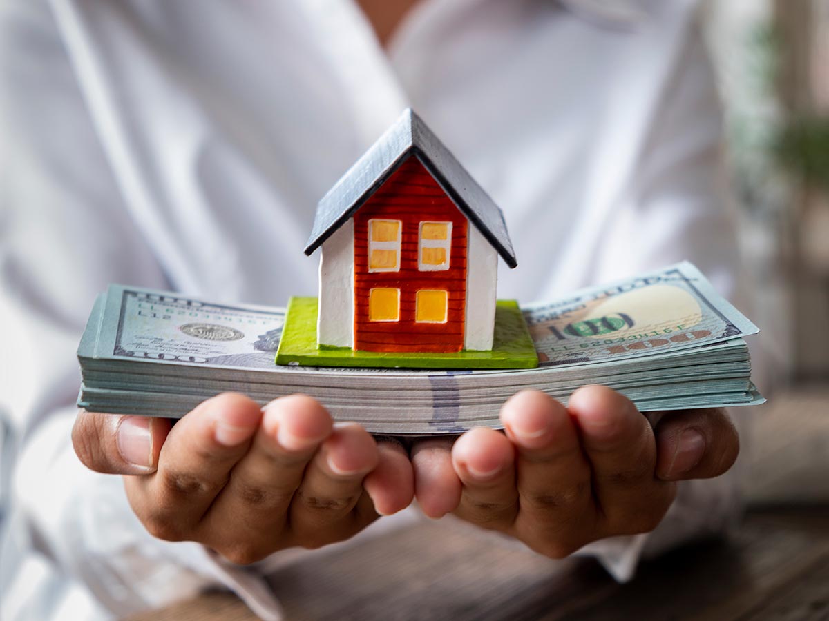 Person holding a stack of cash with a model home on top of it