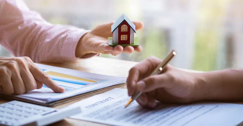 Person holding model home in their hand while another person reads through a home loan contract