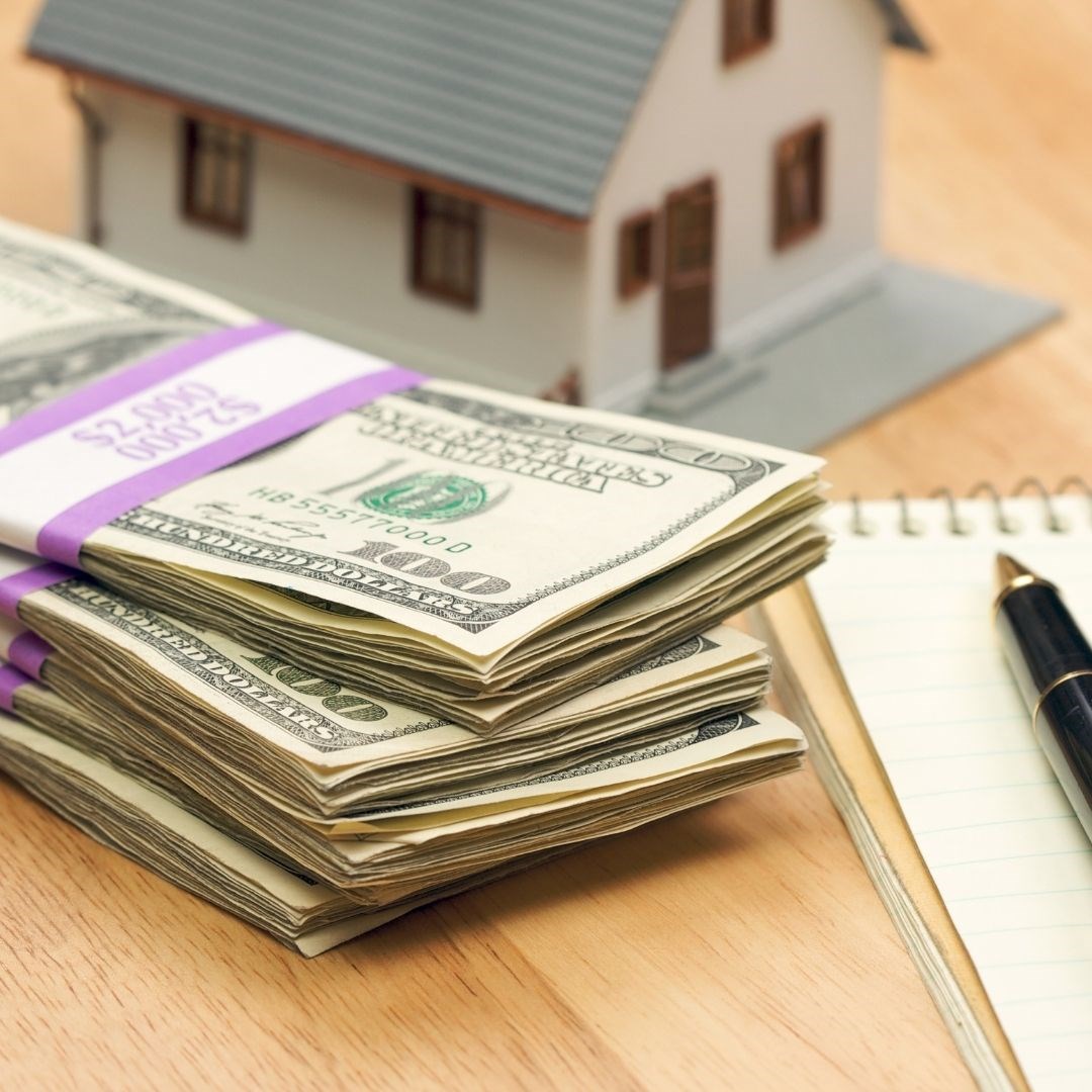 Stack of cash sitting on a table next to a notebook and a miniature house