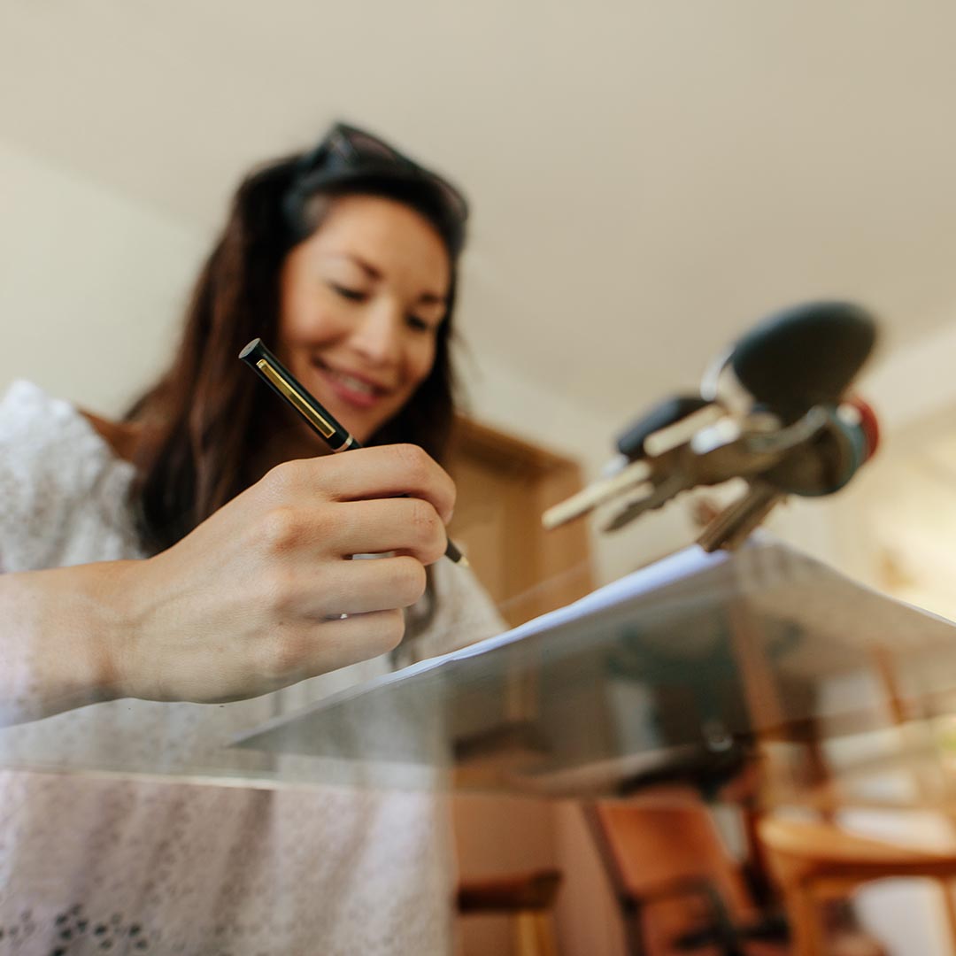 Smiling woman signing paperwork next to a set of keys