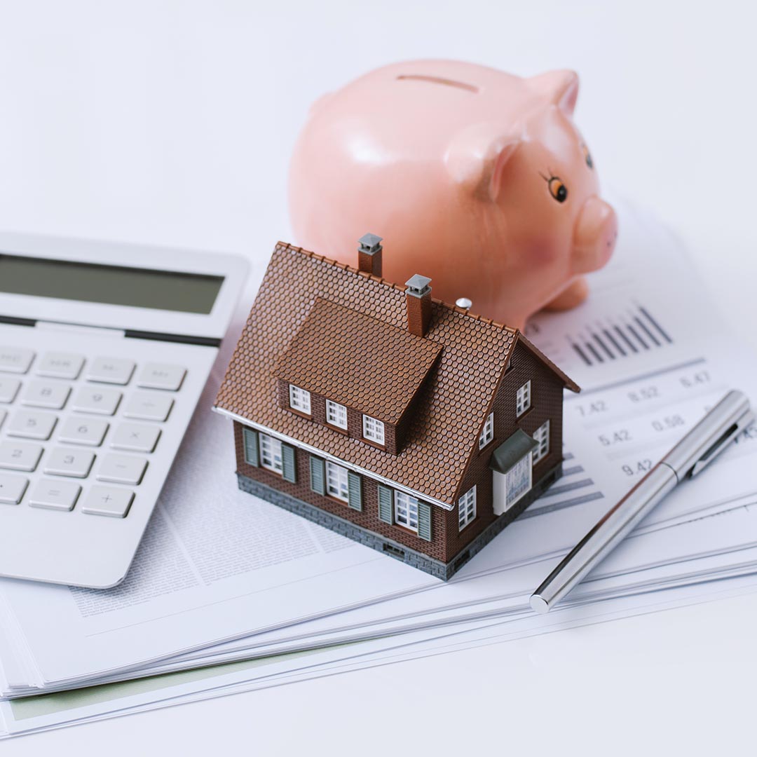 Piggy bank next to a calculator, miniature house and a pen