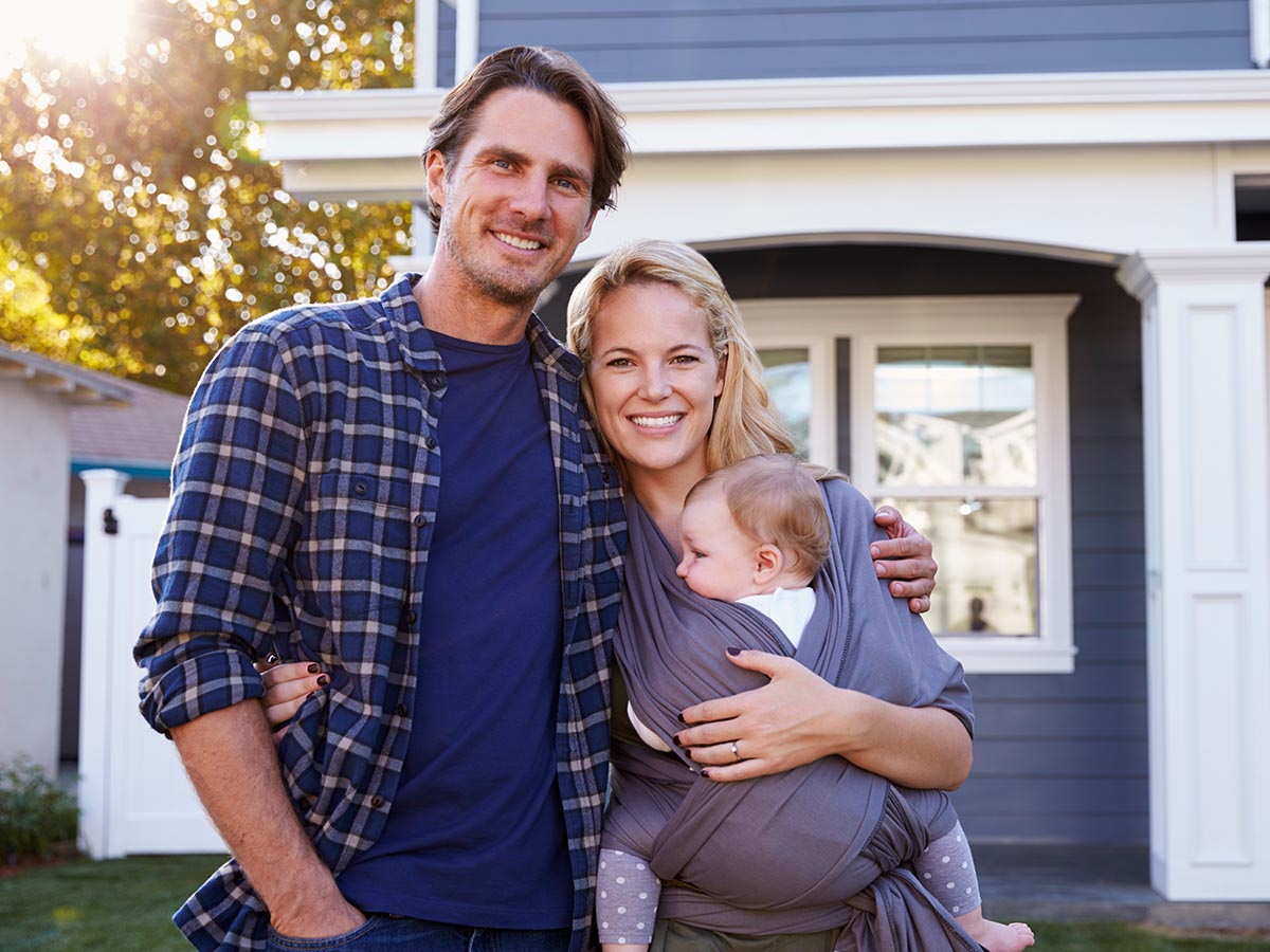 Happy couple with baby standing in front of home