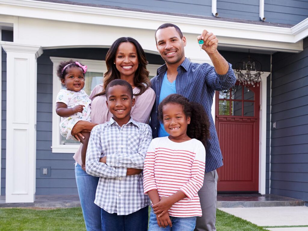 Happy family holding up house keys in front of a blue house