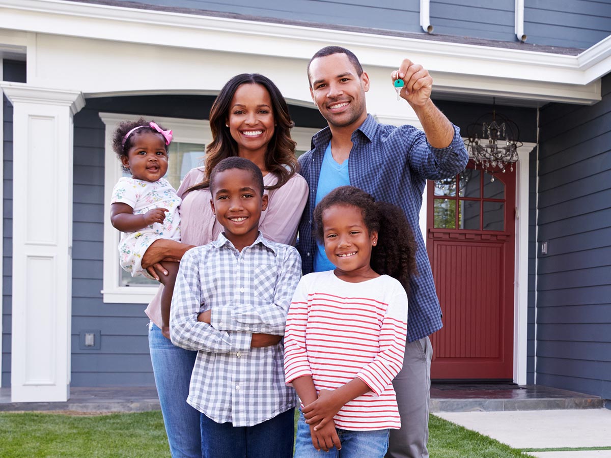 Happy family holding up house keys in front of a blue house