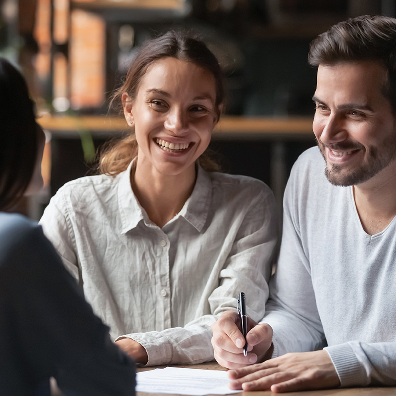 couple signing forms, smiling at loan officer