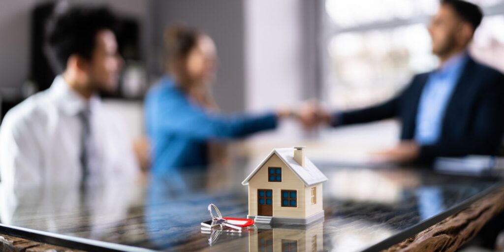 People shaking hands next to a house figurine