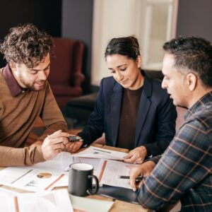 Three people talking around a table with paperwork on it