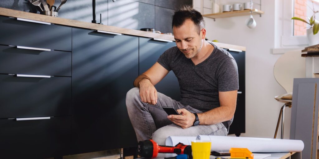 man sits in kitchen looking at phone screen