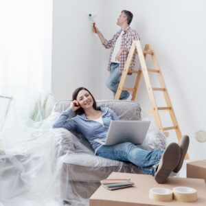 woman sits in chair while man paints wall behind her