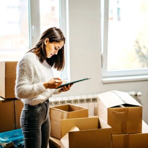 woman looks at clipboard with boxes on the floor 