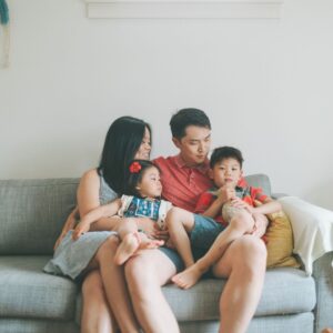 family with 2 kids sits together on grey fabric couch