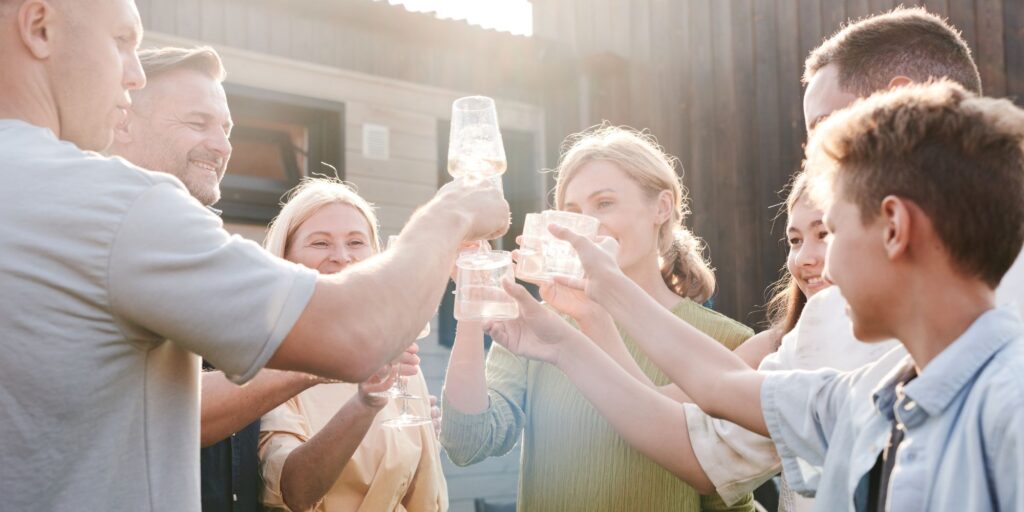 group of people stand outside house clinking drink glasses together