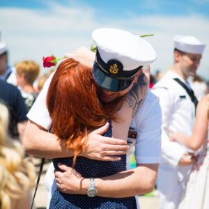 a couple embraces with people in navy uniforms at ceremony