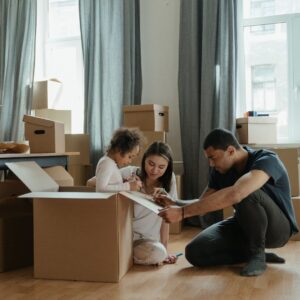 man woman and child sit on floor with moving boxes and draw on cardboard together 