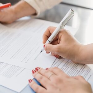 person's hands with red painted nails holds pen to sign paperwork 