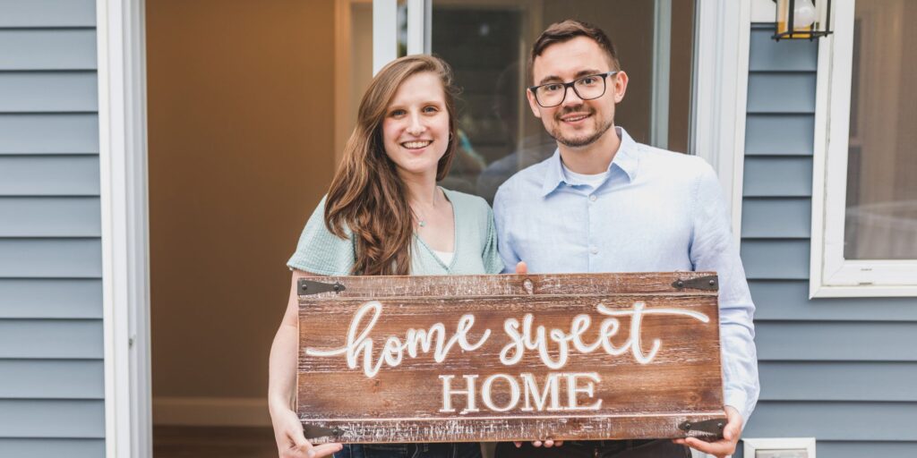 Couple holds Home Sweet Home sign in front of house
